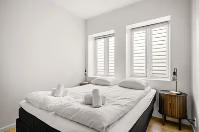 a white bedroom with a large bed with two windows at Light & Modern, City Apartment in Bergen