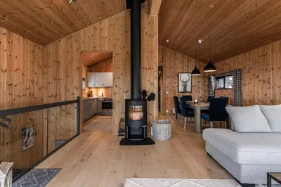 a living room and kitchen with a wood paneled wall at Moderne leilighet i Vestlia-Ski in ski out in Geilo