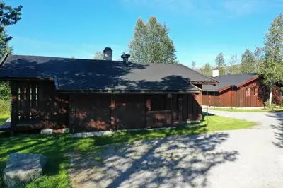 a brown barn with a driveway next to a house at Tvilsombu, cosy cabin close to ski slopes in Geilo