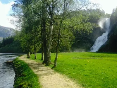 a path next to a river with a waterfall at Renovated Cabin By Lake Djupedal in Bygstad