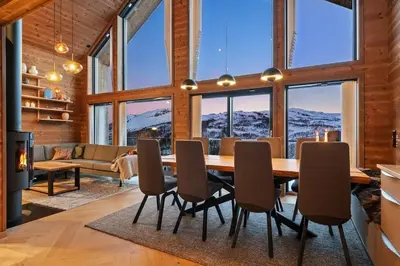 a dining room with a table and chairs and windows at Panoramahytte med fjellutsikt in Sogndal
