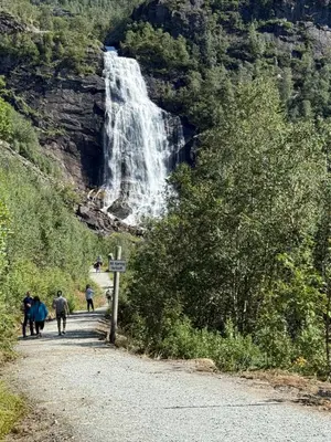 a group of people walking down a road in front of a waterfall at Fossen bratte chalet in Eikedalen