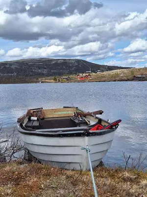 a white boat sitting on the shore of a lake at Fiskebu at Flaksjøen in Venabygd