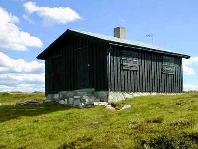 a black building on a hill in a field at Hyggelig fiskebu ved Langrumpa fiskevann in Venabygd