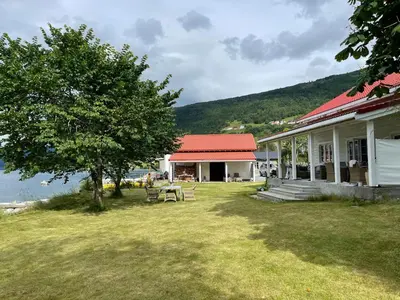 a building with a table and a tree in the yard at Charming house by the fjord in Utvik