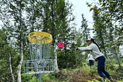 a woman throwing a frisbee into a metal basket at New cabin in Slåseterlia at Skeikampen in Svingvoll