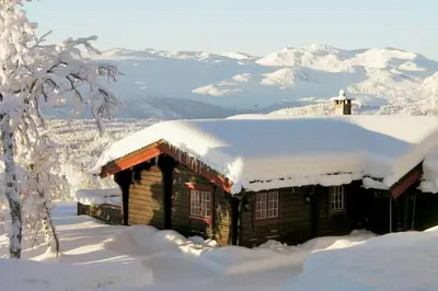 a log cabin covered in snow with mountains in the background at Timber Cabin With Mountain View in Beitostøl