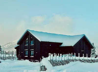 a black barn covered in snow with a fence at Modern Mountain Cabin With Views In Hovden in Hovden