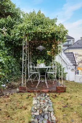 a table and chairs in a garden with a hedge at Lysthuset den lille villa - authentic wodden house in Bergen