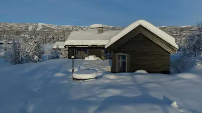 a house covered in snow with a pile of snow at Moderne storhytte med 5 soverom og 3 bad in Beitostøl