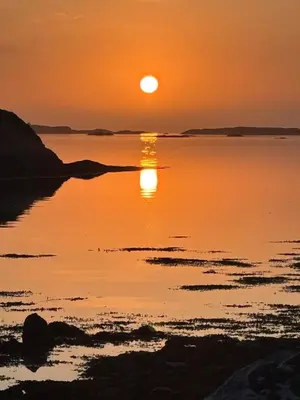 a sunset over a body of water with the sun setting at Strand huset in Hitra