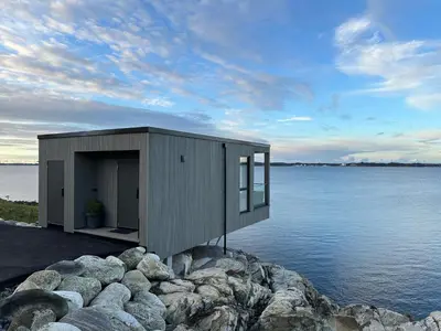 a small building on the edge of a body of water at Hideaway Herdla luxurious cabins 15 m above the sea in Herlø