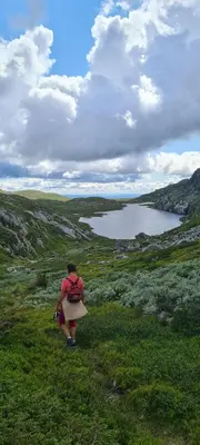 a woman walking on a grassy hill with a lake at Modern mountain cabin with panorama view in Eggedal