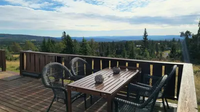 a wooden table and chairs on a deck with a view at Historic Cabin From 1906 In Sjusjøen in Sjusjøen