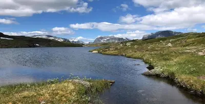 a river in a field with mountains in the background at Log Cabin By Hardangervidda National Park in Nesland