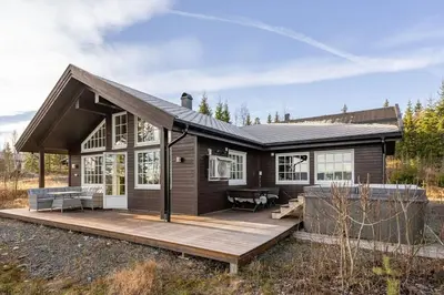 a small house with a wooden deck in a field at Jantelaaven in Trysil