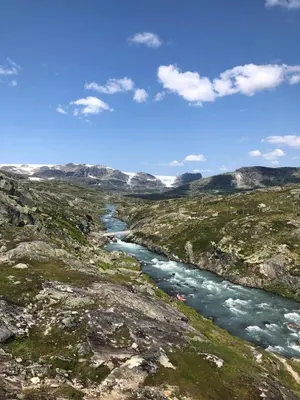 a river in the middle of a field with mountains at Fjellperlen, Hardangervidda in Eidfjord