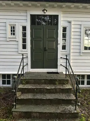 a green door on a white house with stairs at Historic villa with large garden in Stord