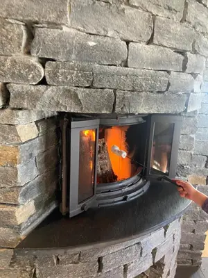 a stone fireplace with a person holding a stick at Rustik hytte i Gausta, ski in, ski out, 10 beds in Gaustablikk