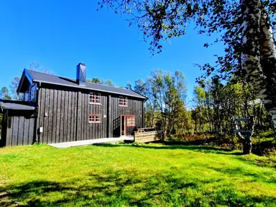 a black barn with a grassy yard in front of it at Trivelig og romslig hytte nær Røros, rikelig med uteplass in Glåmos