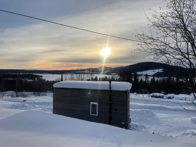 a small shed in the snow with the sun in the sky at Tiny house on wheels with great views Sjusjøen in Mesnali