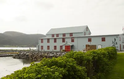 a white building with red doors next to a body of water at Gunnabuda in Longva