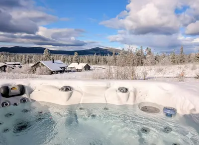 a hot tub in the snow with a house in the background at Winter cabin with Jacuzzi in Trysil