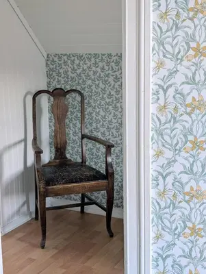 a wooden chair sitting in a room with wallpaper at Lundenhuset 1917 - historic house in the heart of Ulsteinvik in Ulstein