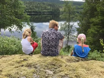 a man and two girls sitting on a hill near a lake at Øyungen 2 in Namsos