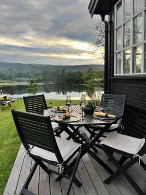 a table and chairs on a deck with a view of a lake at Modern Cottage With River Frontage Near Opphus in Rena