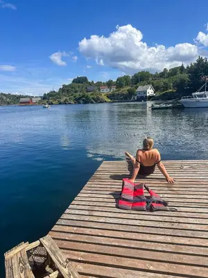 a man sitting on a dock reading a book at Fishermen's Cabin With Sea View in Bømlo