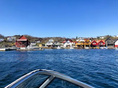 a boat in a body of water with houses at Fishermen's Cabin With Sea View in Bømlo