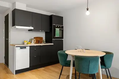 a kitchen with black cabinets and a table with green chairs at Studio apartment in city center in Bergen