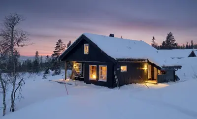 a small cabin in the snow with lights on at Cozy family cabin with fireplace and near ski trails in Lii