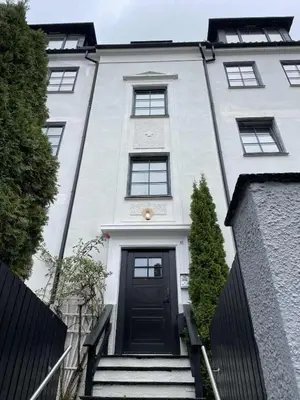 a white house with a black door and stairs at Nice and central apartment in Sandviken with sea view in Bergen