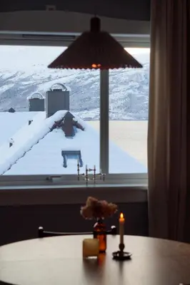 a table with a lamp and a window with snow at Charming apartment with balcony and view! in Ålesund