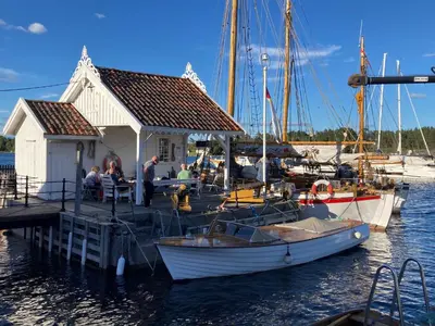 a group of people sitting at a dock with a boat at Langesund brygge in Lii