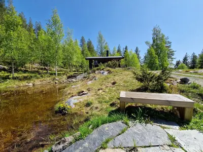 a wooden bench sitting on a hill next to a river at Smia cabin , A Unique Rustic Hideaway in Lii