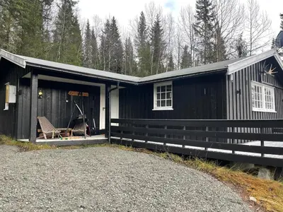 a black building with a porch and a chair in front at Hjemmekoselig Hytte Ved Øyangen in Beitostøl