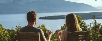 a man and woman sitting on a bench with cups of coffee at Romantic Getaway Hot Tub, Cinema & View in Stange