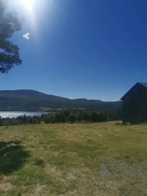 a view of a field with a barn and a lake at Åsrud seter i Jotunheimen in Randsverk