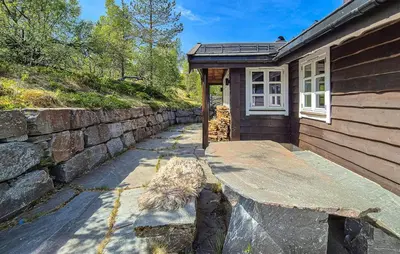 a house with a stone wall next to a sidewalk at Cosy Cabin With Jacuzzi Right By The Ski Slope in Norheimsund