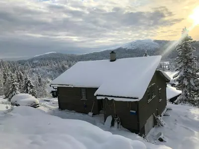 a cabin with snow on the roof in the mountains at Unique Cabin And Freestanding Sauna With Views in Aurdal