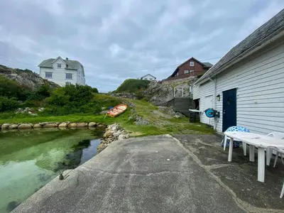 a house with a table and a boat in a river at Seafront House From 1952 With Views In Veivåg in Bekkjarvik