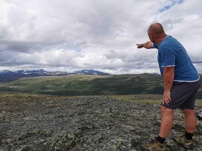 a man standing on top of a mountain pointing at Live in the realm of the musk oxen on Dovrefjell in Hjerkinn