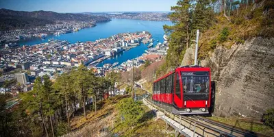 a red train on the tracks next to a river at Central apartment with parking in unique surroundings in Bergen