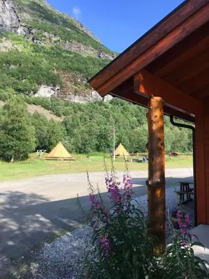 a building with a view of a field with tents at Dalen Gaard camping og hytter in Geiranger