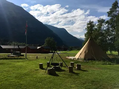 a tent in a field with mountains in the background at Dalen Gaard camping og hytter in Geiranger