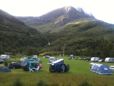 a group of tents in a field with a mountain at Dalen Gaard camping og hytter in Geiranger