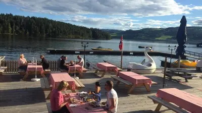 a group of people sitting at tables on a dock on a lake at Steinvik Camping in Moelv